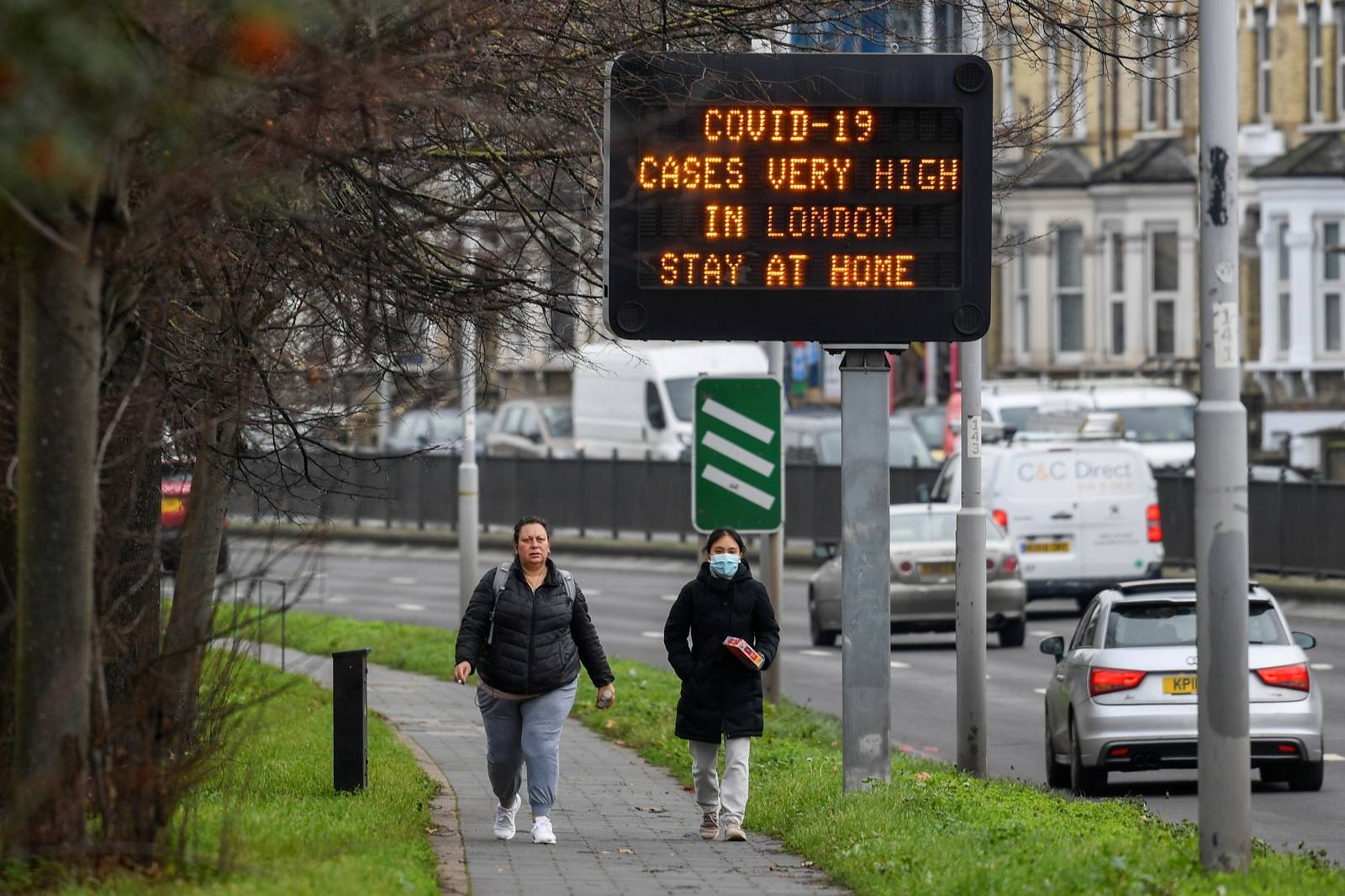 People walk past a roadside public health information sign, amidst the coronavirus disease (COVID-19) pandemic, in London
