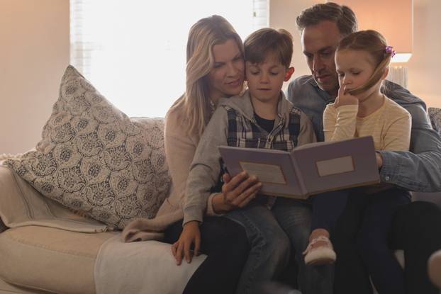 Front view of Caucasian family of four reading story book in living room at home