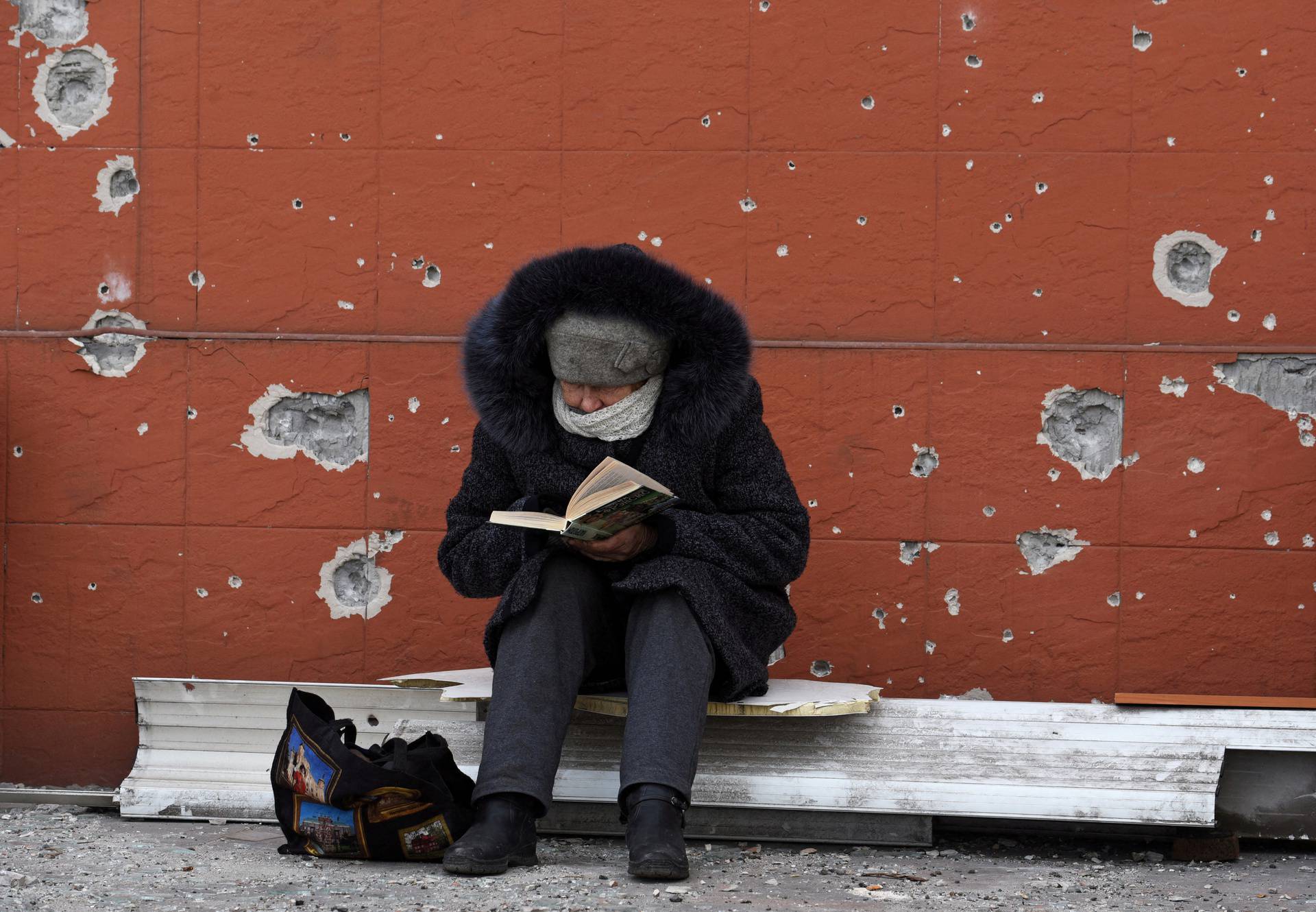 A local resident reads a book near a damaged building in Mariupol