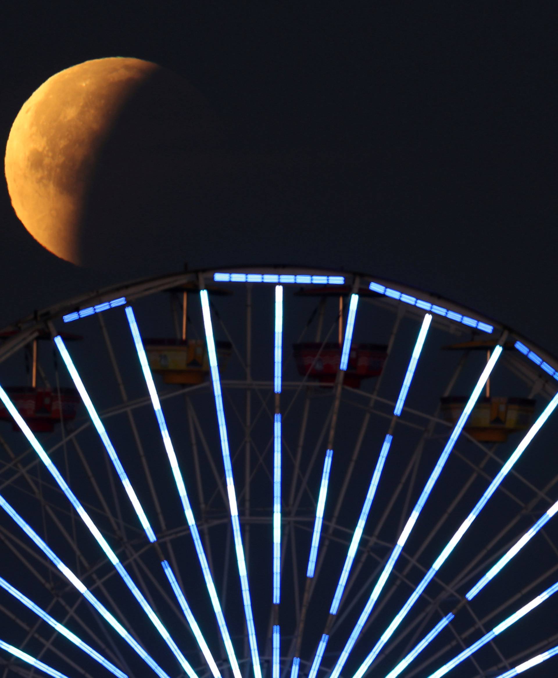 A lunar eclipse of a full "Blue Moon" is seen above the ferris wheel on the Santa Monica Pier in Santa Monica