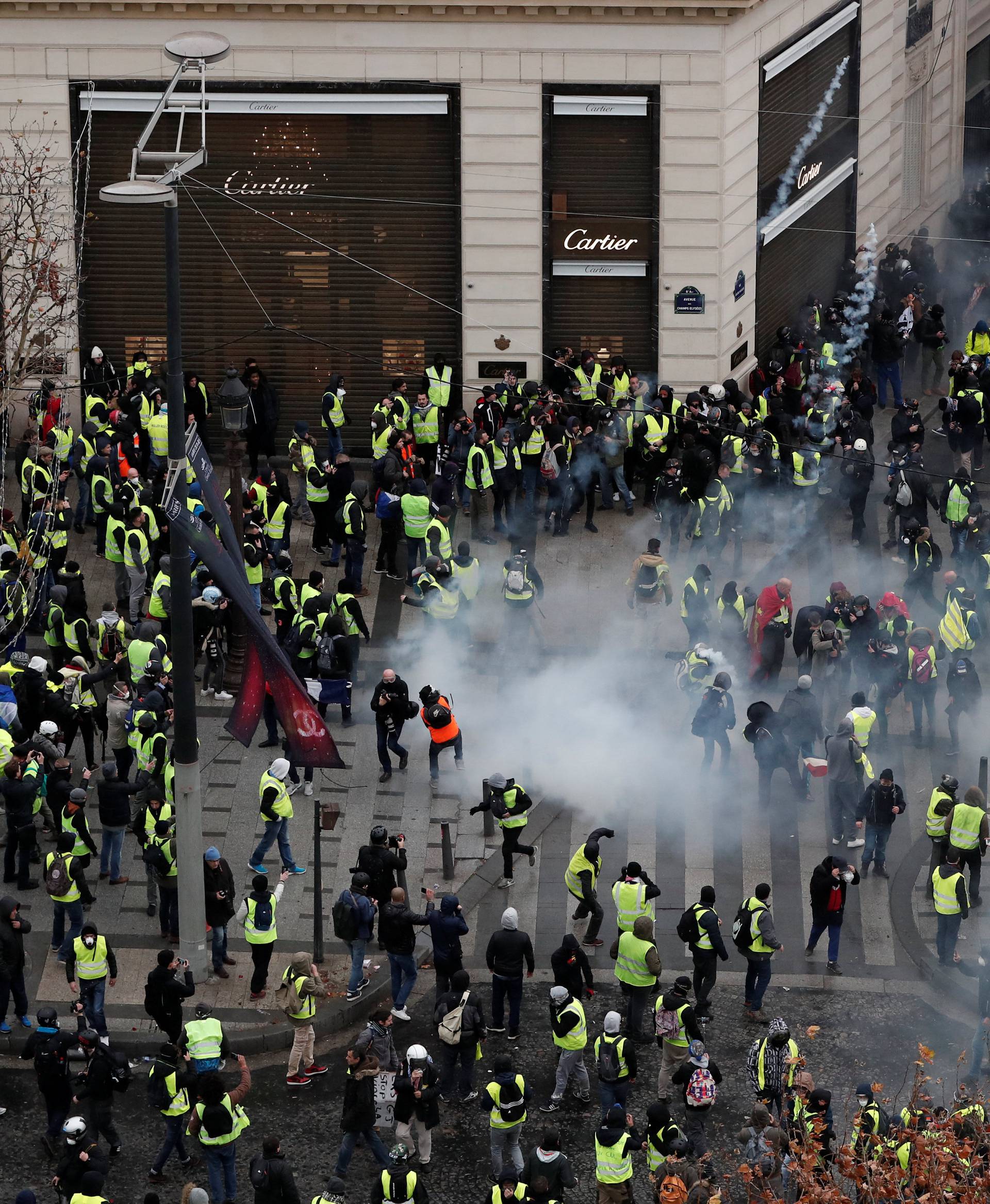 Tear gars floats in the air around protesters wearing yellow vests during clashes with French Gendarmes on the Champs-Elysees Avenue in Paris