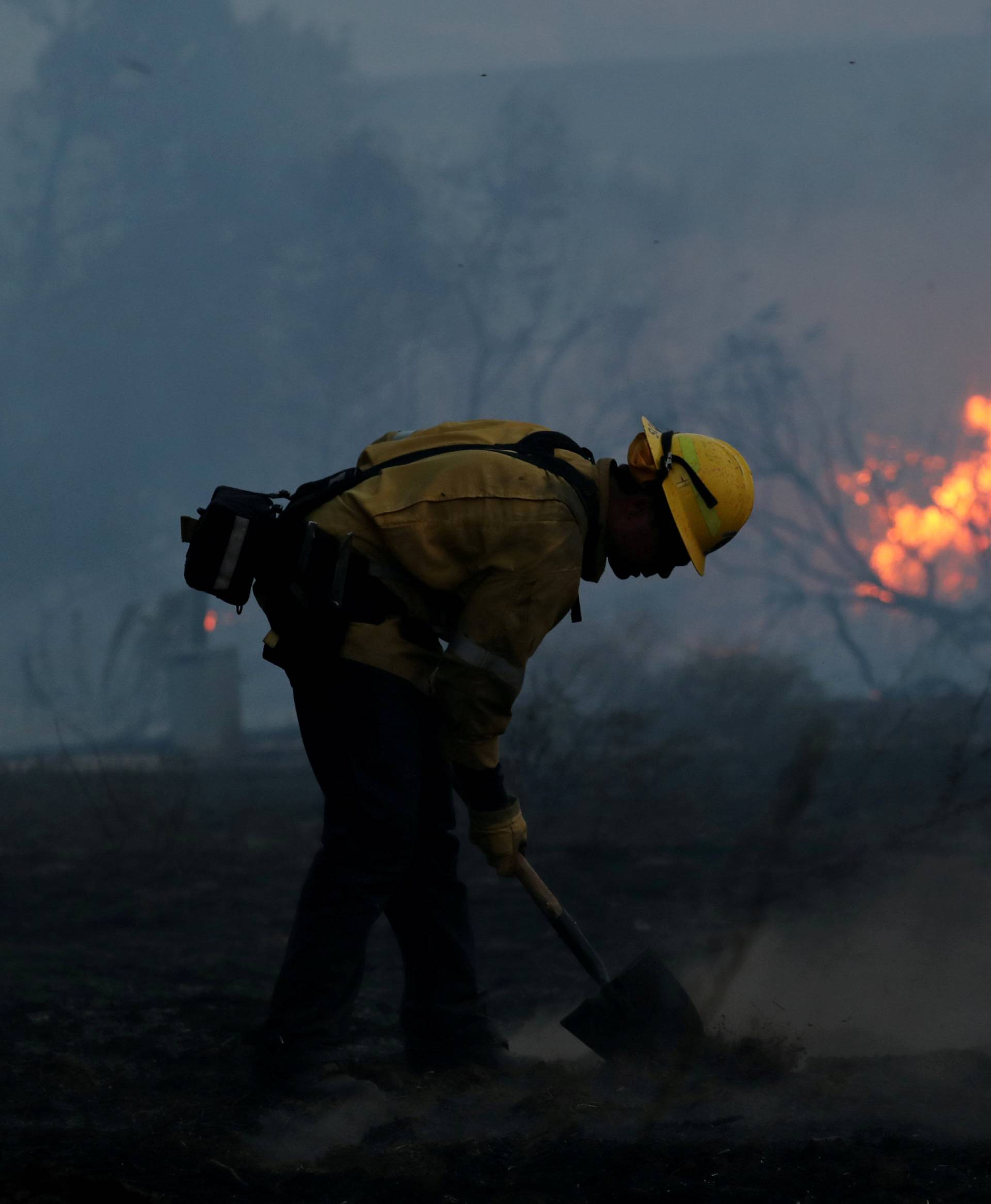 A firefighter works to put out hot spots on a fast moving wind driven wildfire in Orange, California