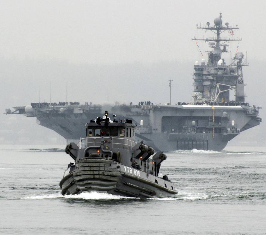 The Nimitz-class aircraft carrier USS Abraham Lincoln (CVN 72) departs Naval Station Everett, Washington, on a scheduled seven-month deployment to the U.S. 5th Fleet area of responsibility, with tugboats assisting in pier operations and ship maneuvering.
