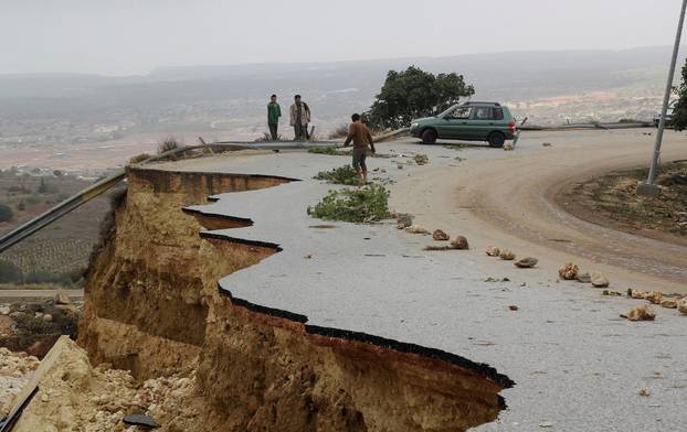 People stand in a damaged road as a powerful storm and heavy rainfall flooded hit Shahhat city