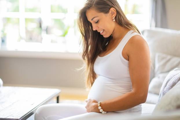 Smiling pregnant woman lying on the sofa touching her belly