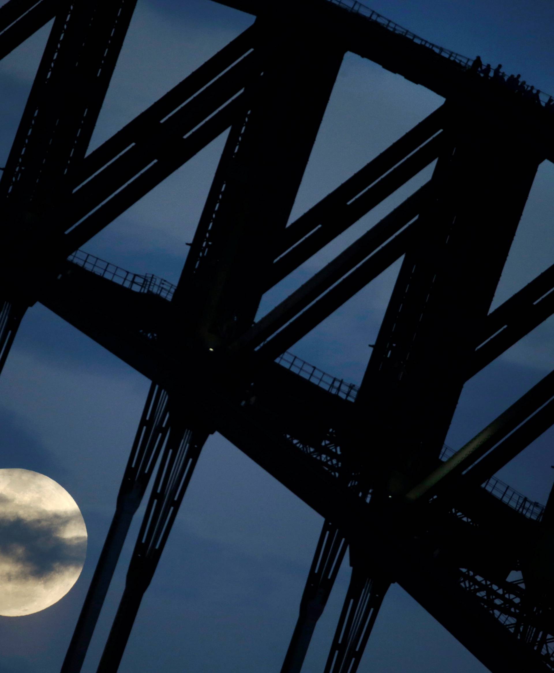 Participants in a Sydney Harbour Bridge Climb walk down the western span of the famous Australian landmark as the Super Moon rises through clouds after sunset