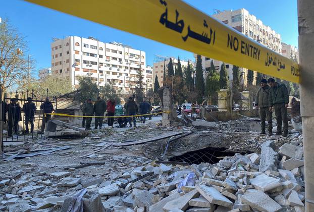 Police officers stand on the rubble of a damaged building at the site of a rocket attack, in central Damascus' Kafr Sousa neighborhood