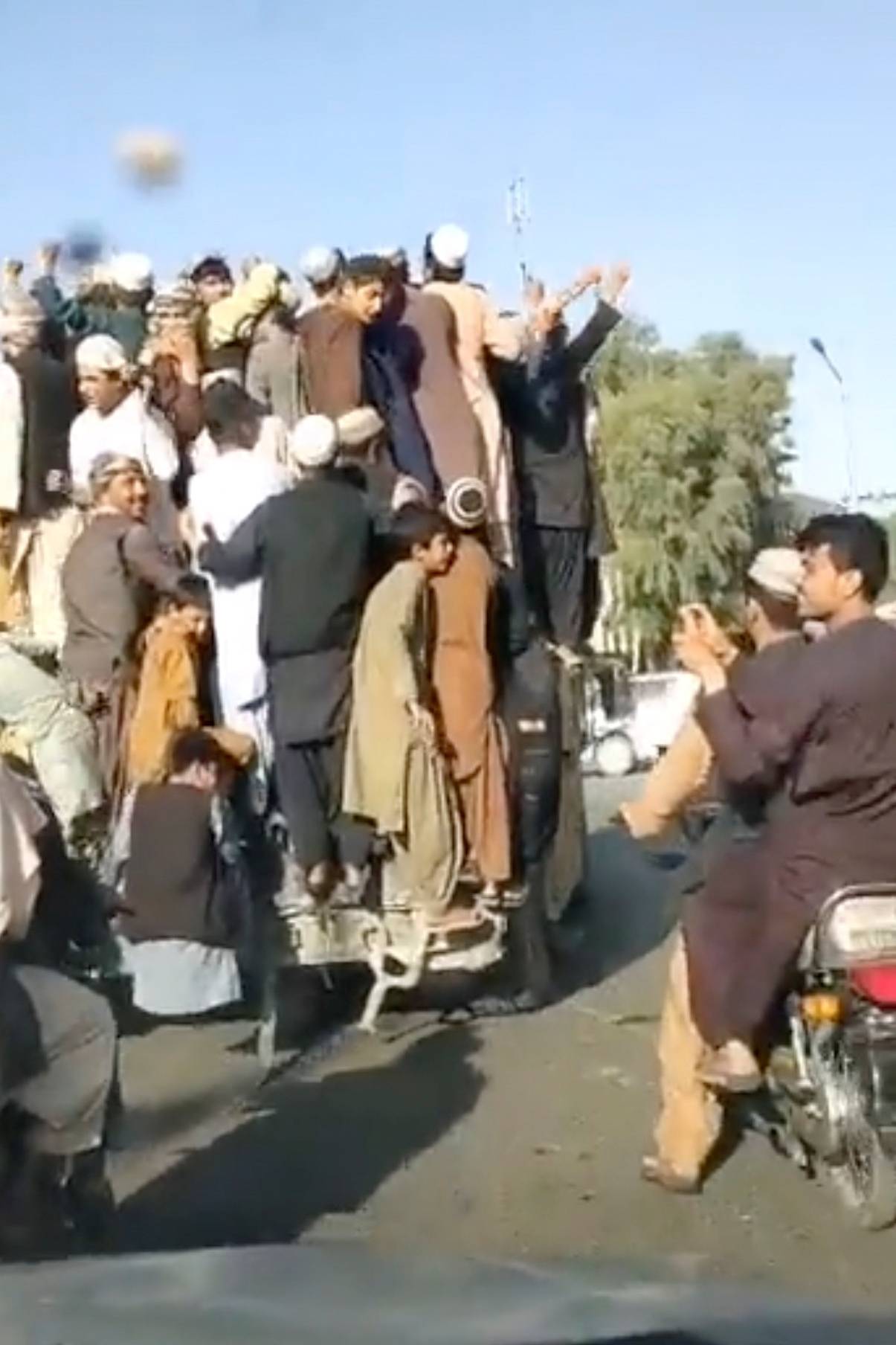 People stand atop an armored vehicle as it drives through Shaheedan Square, in the city of Kandahar