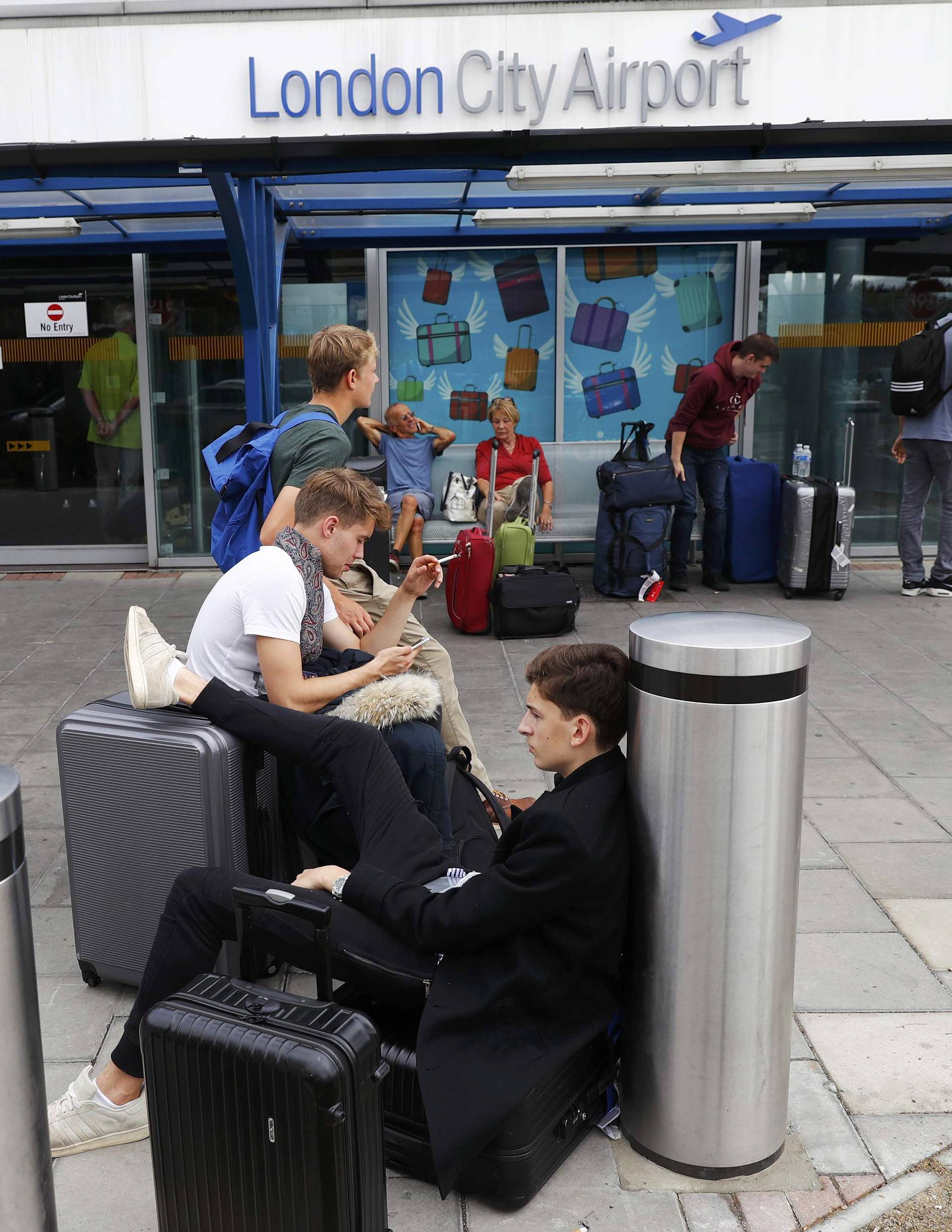 Passengers sit outside City Airport after a protest closed the runway causing flights to be delayed, in London