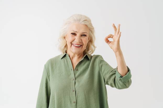 Grey senior woman in shirt smiling and gesturing ok sing