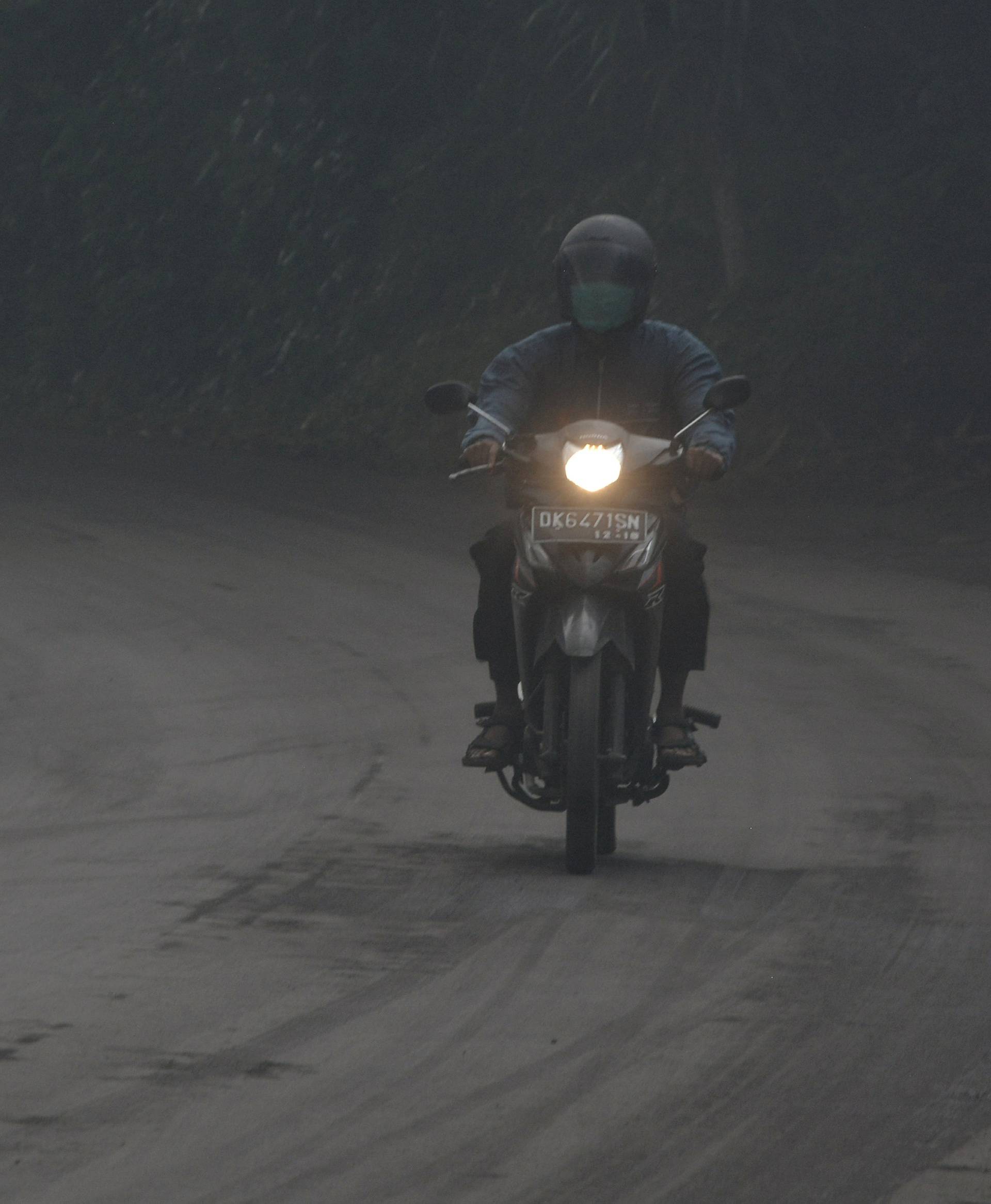 A motorist rides his motorbike during a shower of ash and rain from Mount Agung volcano during an eruption in Bebandem Village, Karangasem, Bali