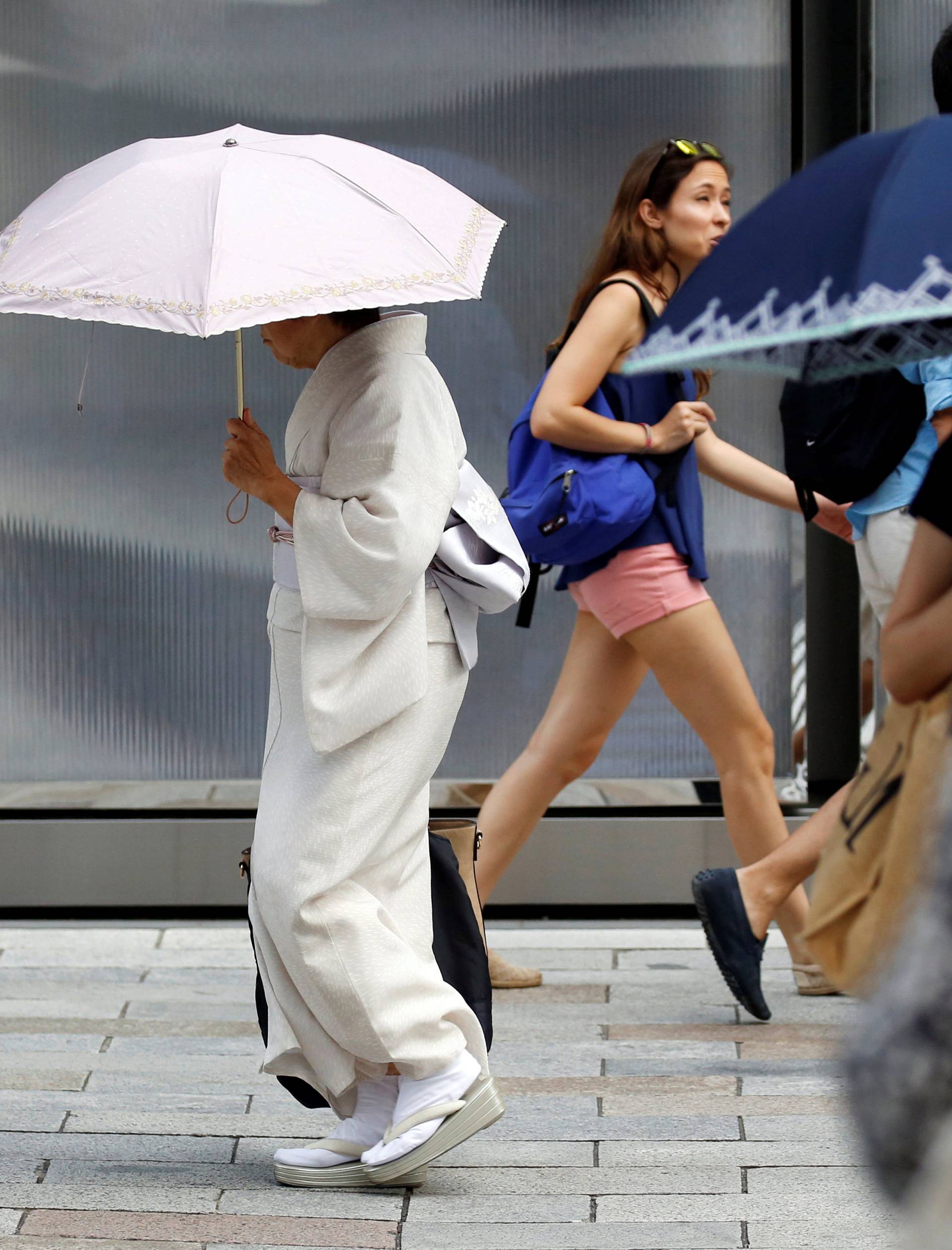 A kimono-clad woman using a sun umbrella walks on a street during a heatwave in Tokyo
