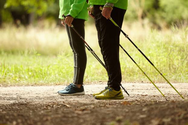 Cropped image of woman and man walking with Scandinavian sticks in autumn forest, outdoors. Nordic walking, healthy lifestyle