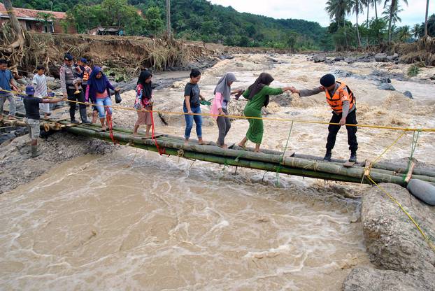 Police officers help people to get through an emergency bridge over the Cidurian river in Bogor, Indonesia