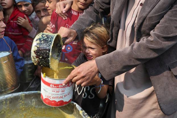 Palestinians gather to receive meals cooked by a charity kitchen, in Deir Al-Balah, central Gaza Strip