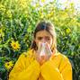Beautiful sexy young woman lies on flowers background. Young girl sneezing and holding paper tissue in one hand and flower bouquet in other. Flu.