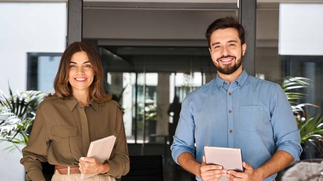 Two,Business,Partners,Executives,Standing,In,Office,Looking,At,Camera.