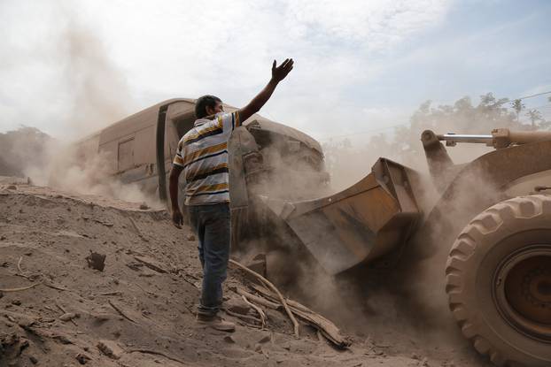 A man gestures as a power shovel removes ash at an area affected by the eruption of the Fuego volcano in the community of San Miguel Los Lotes in Escuintla