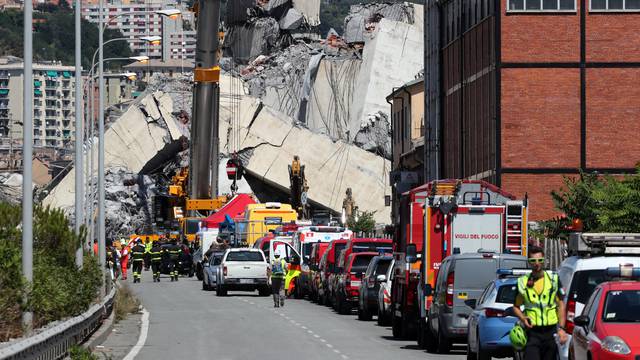 Firefighters and rescue workers stand at the site of a collapsed Morandi Bridge in the port city of Genoa