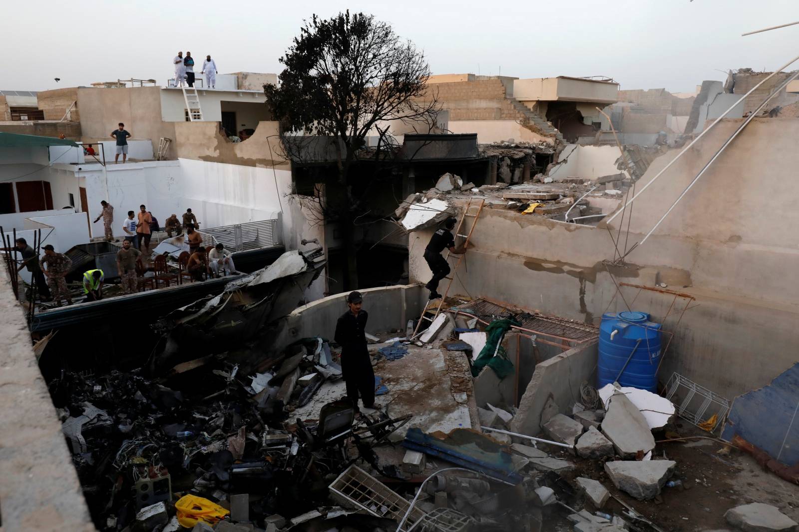 People stand on a roof of a house amidst debris of a passenger plane, crashed in a residential area near an airport in Karachi