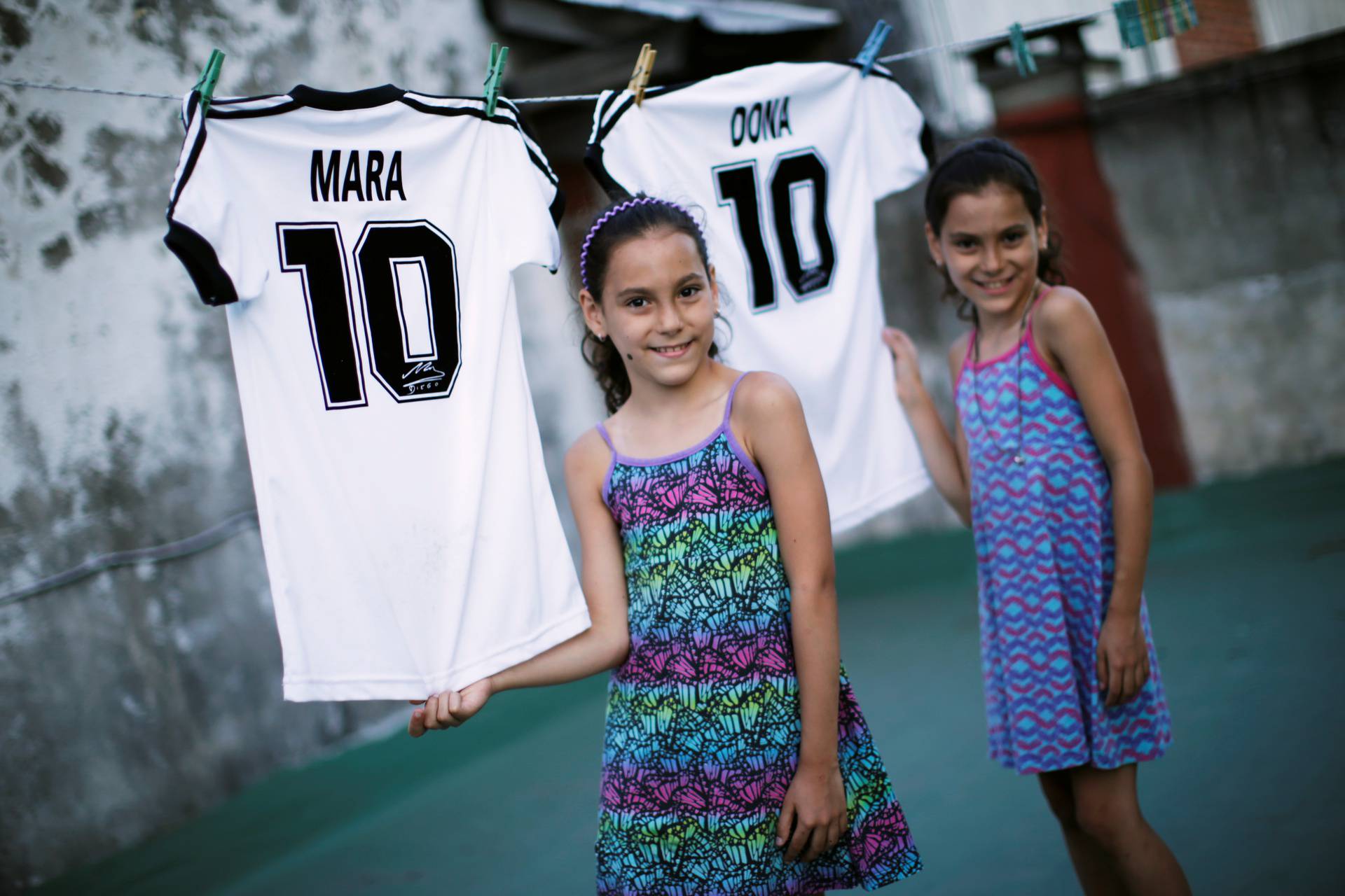 Mara and Dona, twin daughters of Walter Gaston Rotundo,a devoted Diego Maradona fan who named his daughters after the soccer star, stand near t-shirts with their names, in Buenos Aires