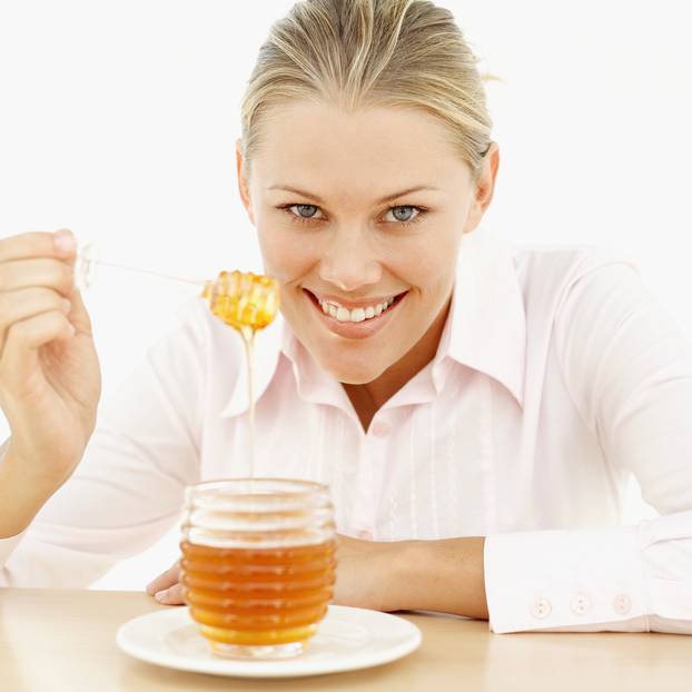 close-up of a young woman holding a honey dipper over a jar of honey