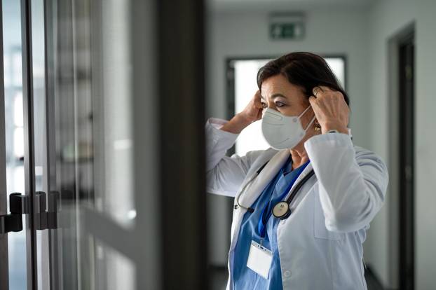 Portrait of senior woman doctor putting on respirator in hospital, coronavirus concept.