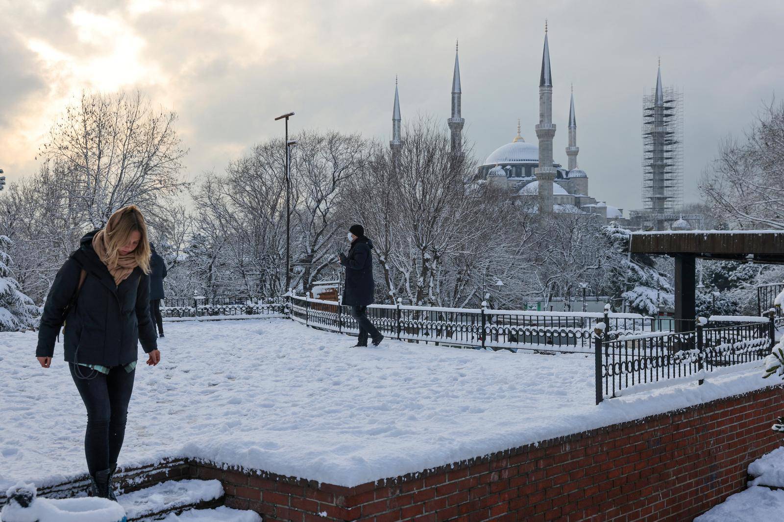 Tourists walk along Sultanahmet Square as Sultan Ahmet Mosque is seen in the background during a snowy day in Istanbul