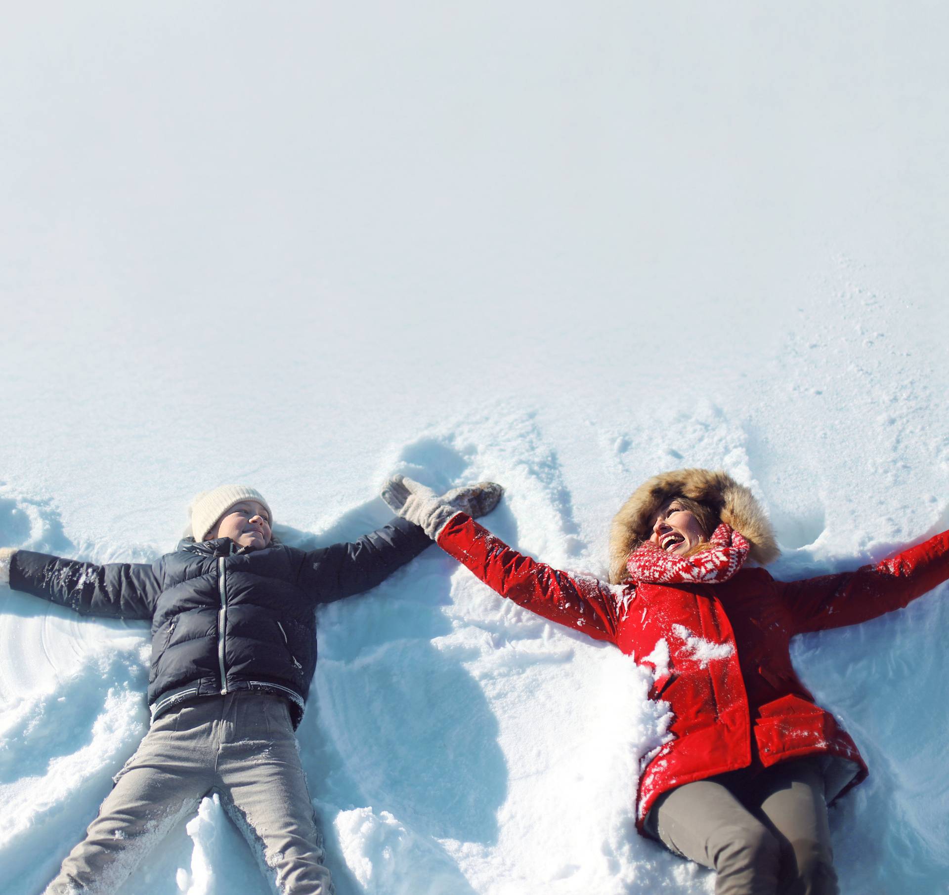 Happy mother, son playing having fun lying in snow winter