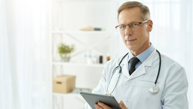 Handsome,Doctor,In,Lab,Coat,Using,Tablet,Computer,In,Clinic