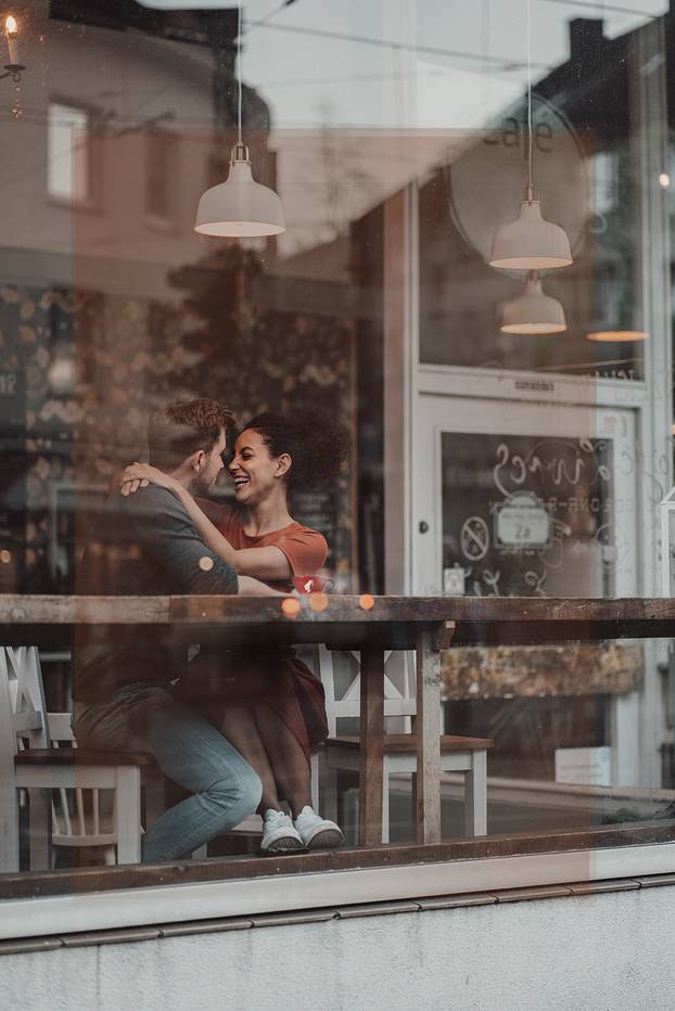 Smiling woman looking at man while sitting with arm around at cafe