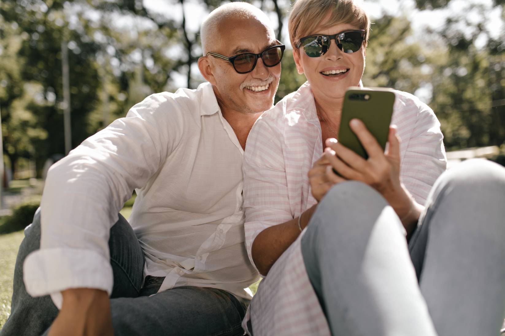 Joyful lady with short hair in sunglasses and striped shirt smiling, holding smartphone and opposin