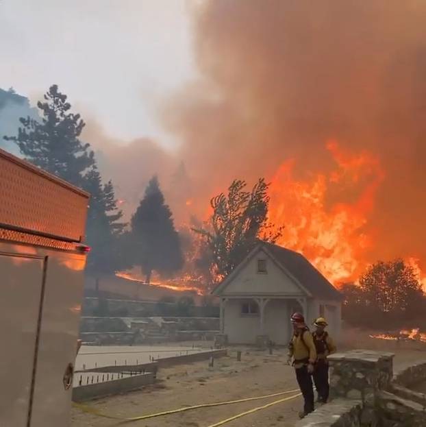 Social media video grab shows firefighters looking at flames raging from uncontrolled wildfires in Oak Glen