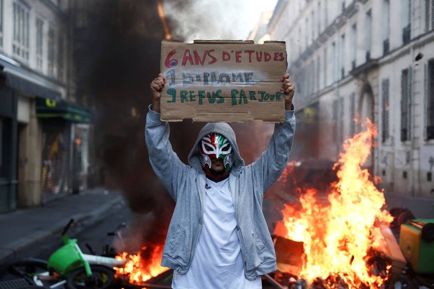 A person wearing a mask holds a placard, the day after a national day of demonstrations against the cost of living and rising fuel prices, in Paris