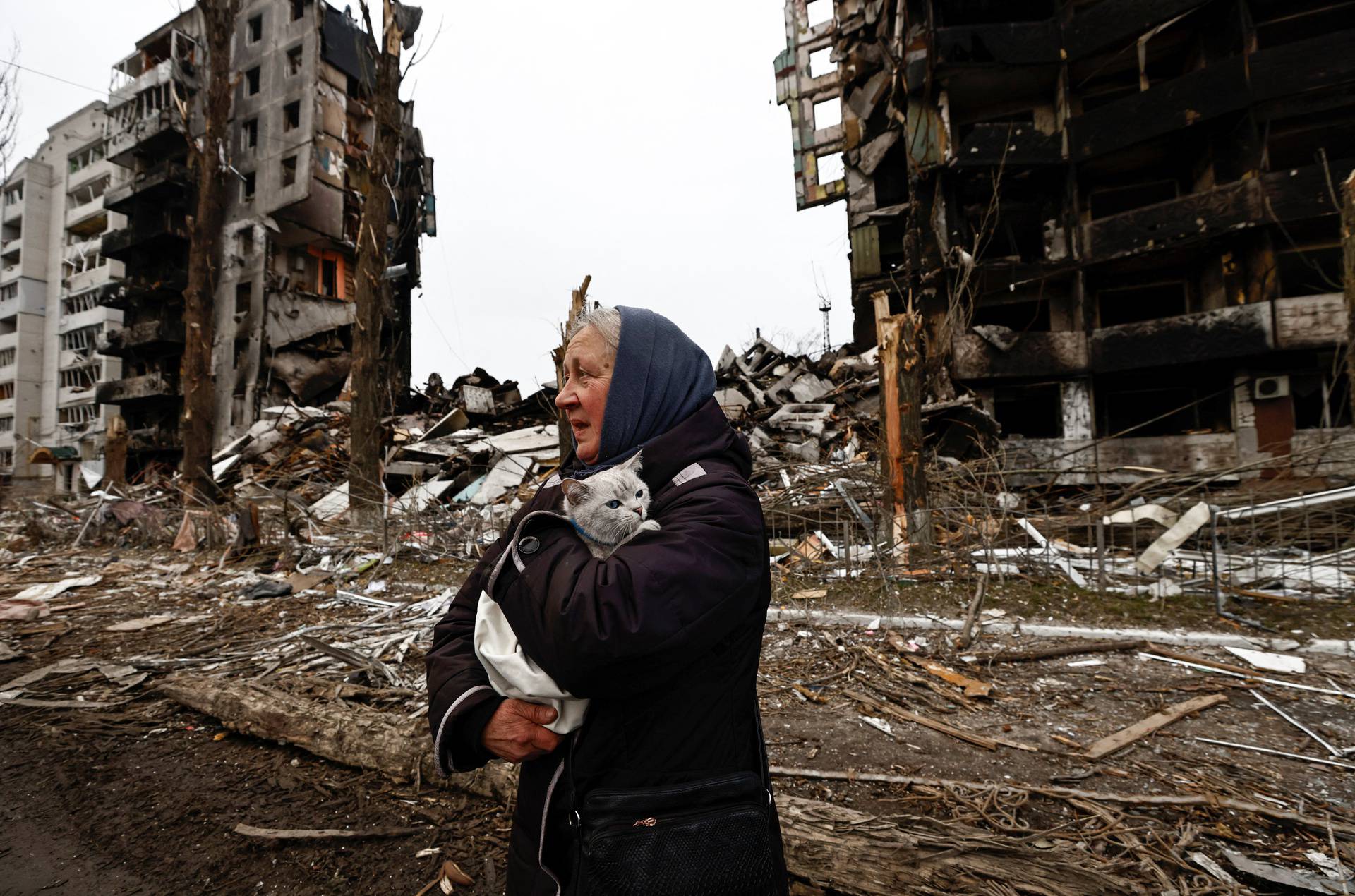 A woman carries her cat as she walks past buildings that were destroyed by Russian shelling