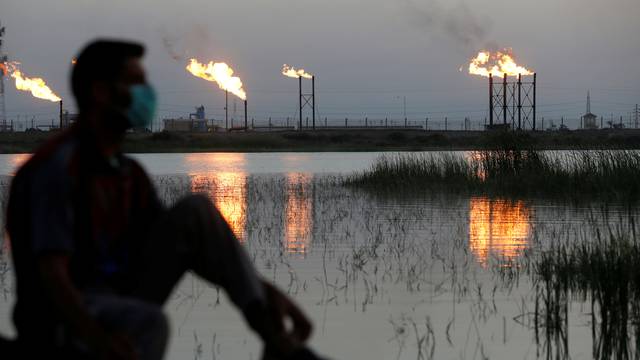 FILE PHOTO: Flames emerge from flare stacks at Nahr Bin Umar oil field, as a man is seen wearing a protective face mask , following the outbreak of the coronavirus, north of Basra