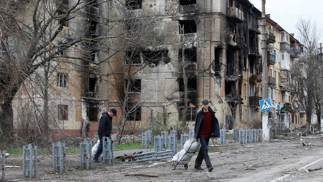 People walk past a damaged residential building in Mariupol