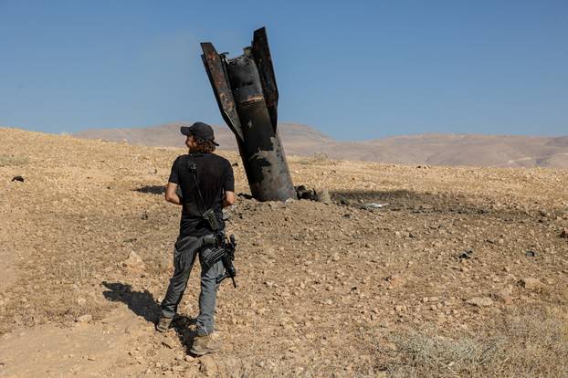 An Israeli settler stands next to part of a missile protruding from the ground, following strikes from Iran, in the central Israeli-occupied West Bank