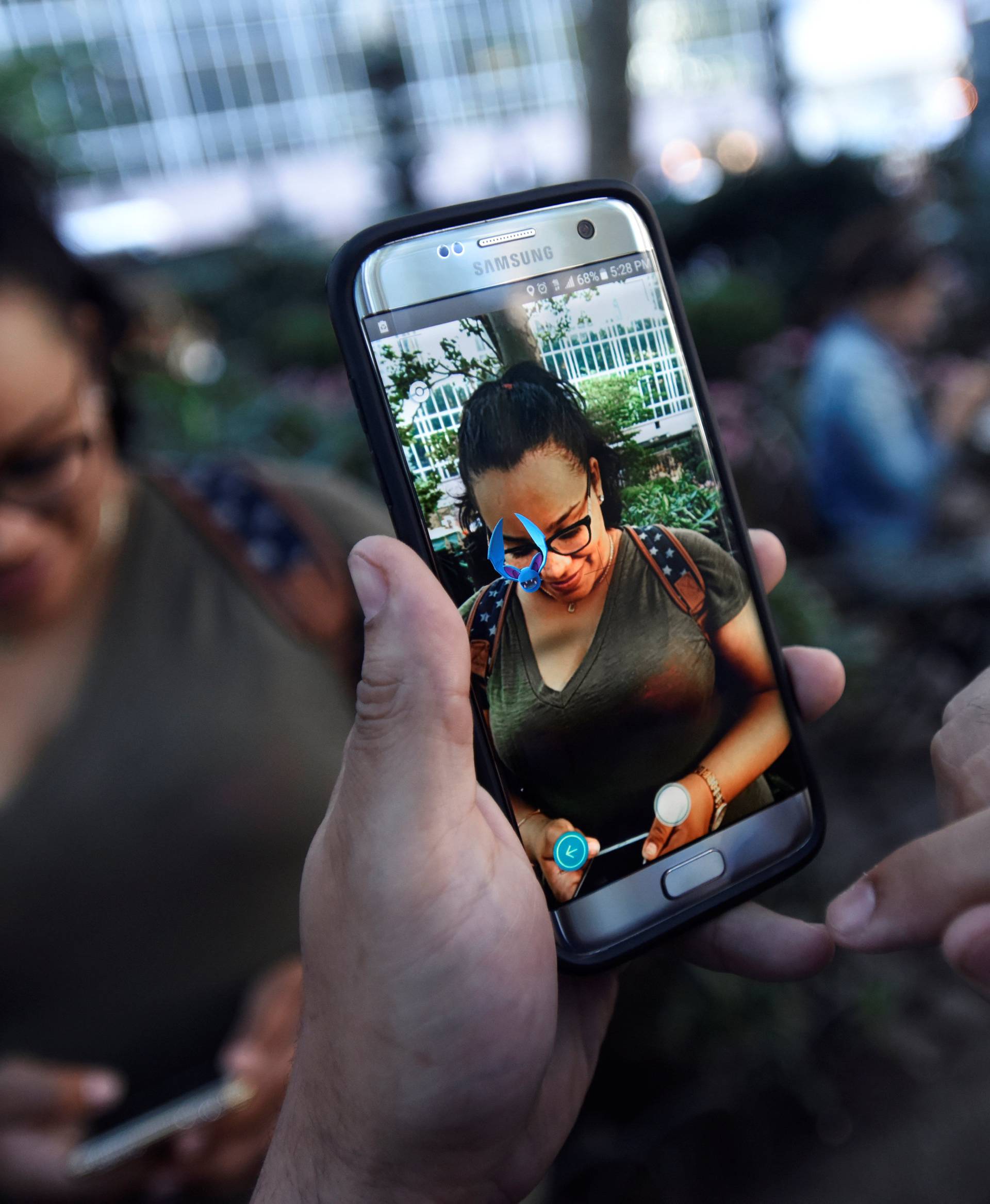 A Pokemon appears on the screen next to a woman as a man plays the augmented reality mobile game "Pokemon Go" by Nintendo in Bryant Park in New York City