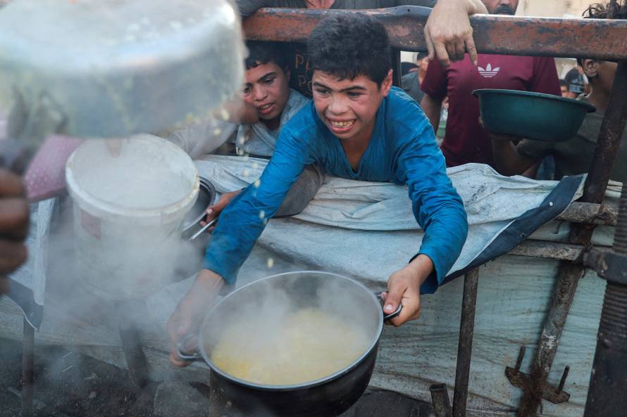 Palestinians wait to receive food from a charity kitchen amid hunger crisis, in Gaza City