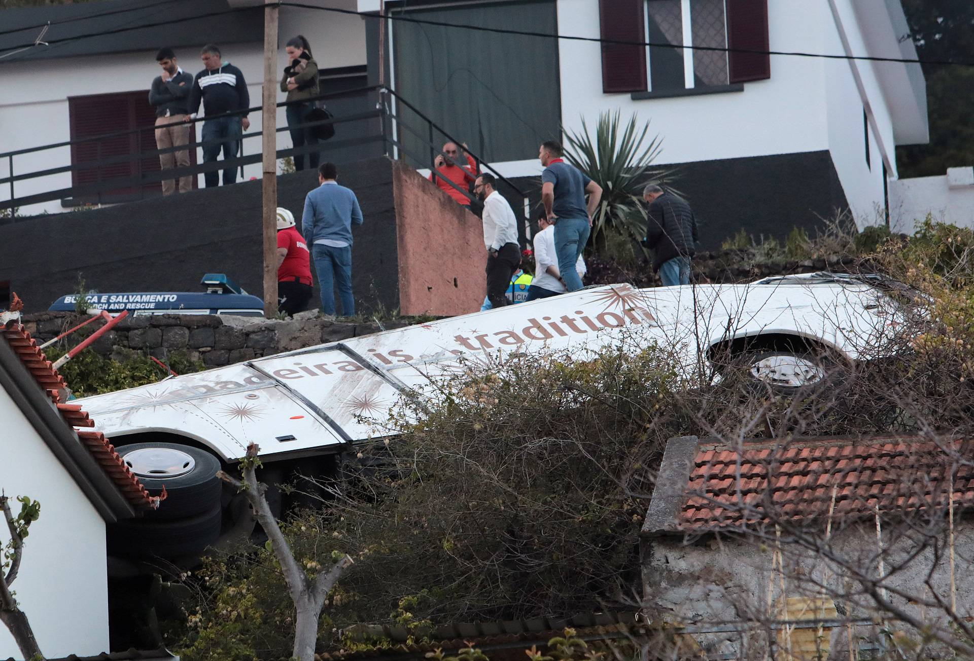 People stand next to the wreckage of a bus after an accident in Canico