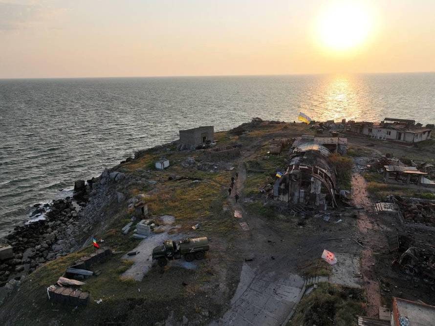 Ukrainian service members walk next to destroyed buildings on Snake (Zmiinyi) Island
