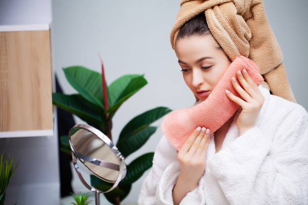 Pretty girl in white coat wipes face with towel after shower