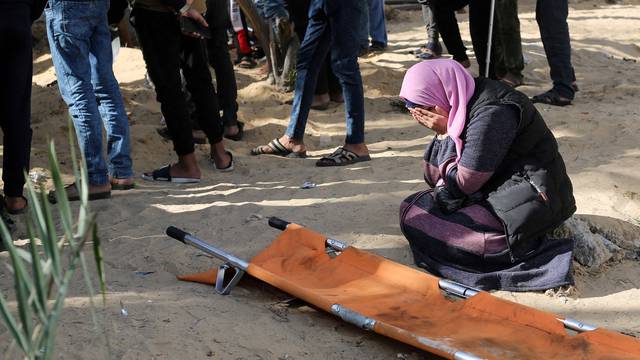 A woman reacts while people bury bodies of Palestinians killed in an Israeli strike, at the Nasser hospital premises