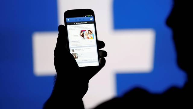 FILE PHOTO: A man is silhouetted against a video screen with an Facebook logo as he poses with an Samsung S4 smartphone in this photo illustration taken in the central Bosnian town of Zenica