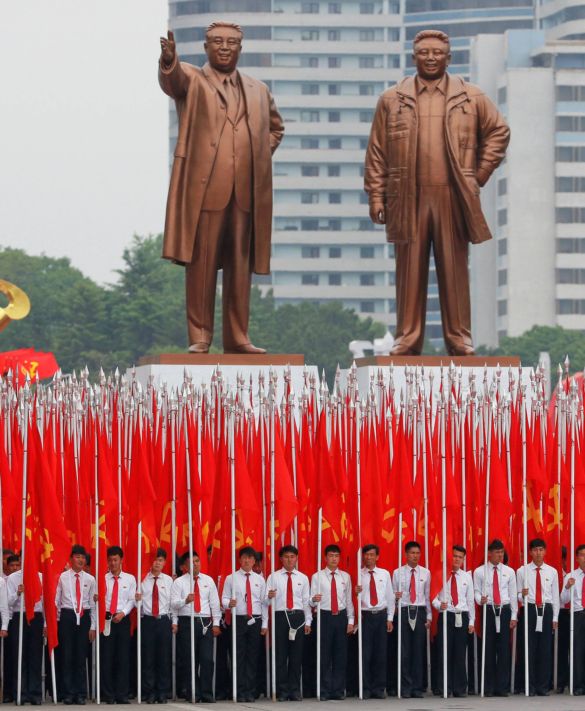 Students carrying party flags stand under statues of former North Korean leaders Kim Il Sung and Kim Jong Il at the beginning of a mass rally and parade in Pyongyang