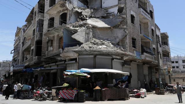 FILE PHOTO: People walk past a damaged building in the city of Idlib