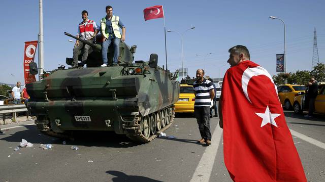A man wrapped in a Turkish flag walks past a military vehicle in front of Sabiha Airport, in Istanbul