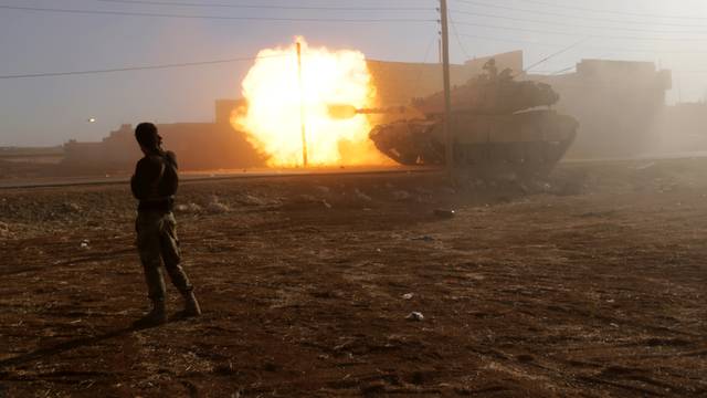 A rebel fighter stands near a Turkish tank as it fires towards Guzhe village, northern Aleppo countryside