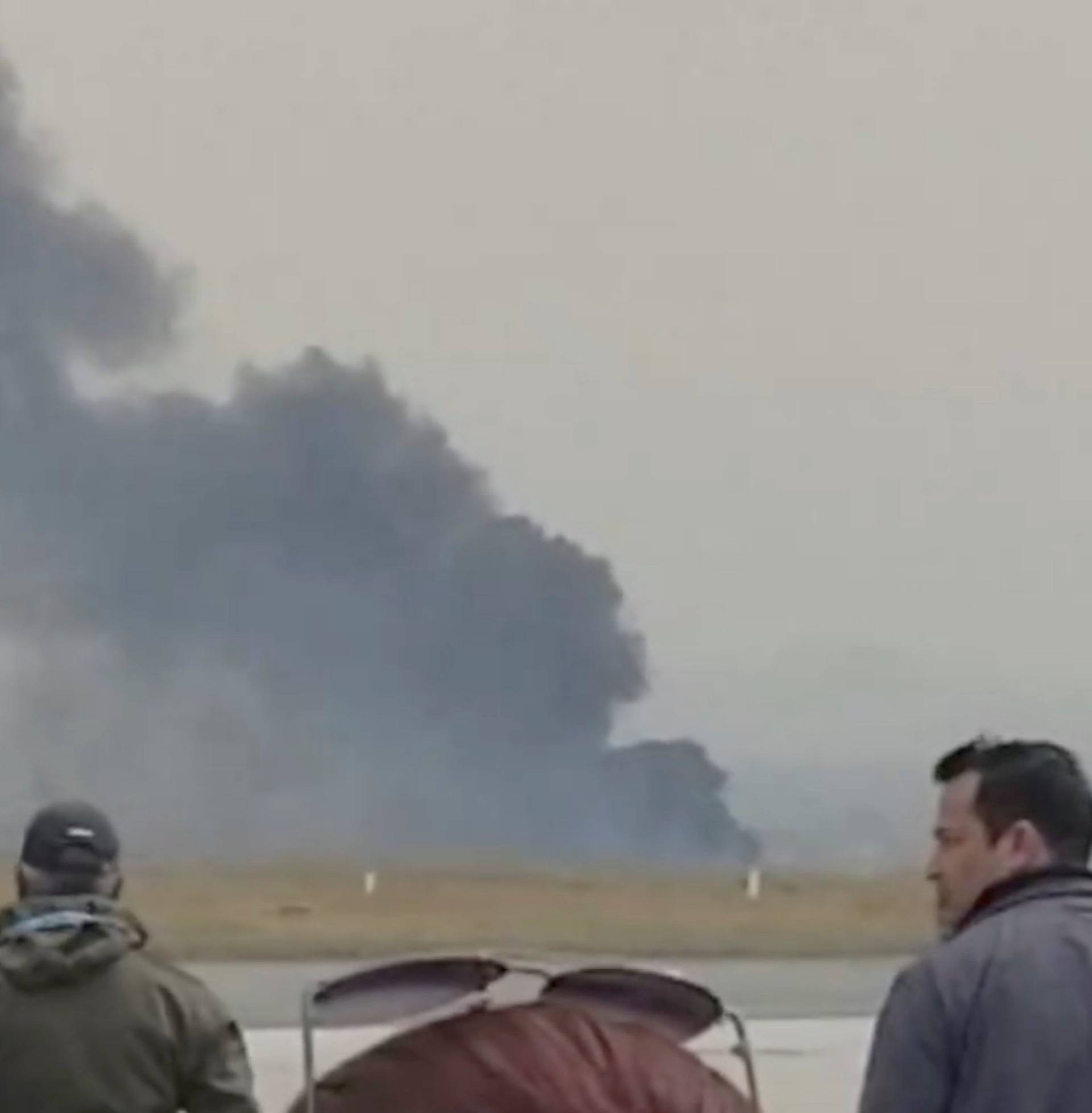 People stand as smoke rises following the crash of a Bangladeshi aircraft at Kathmandu airport